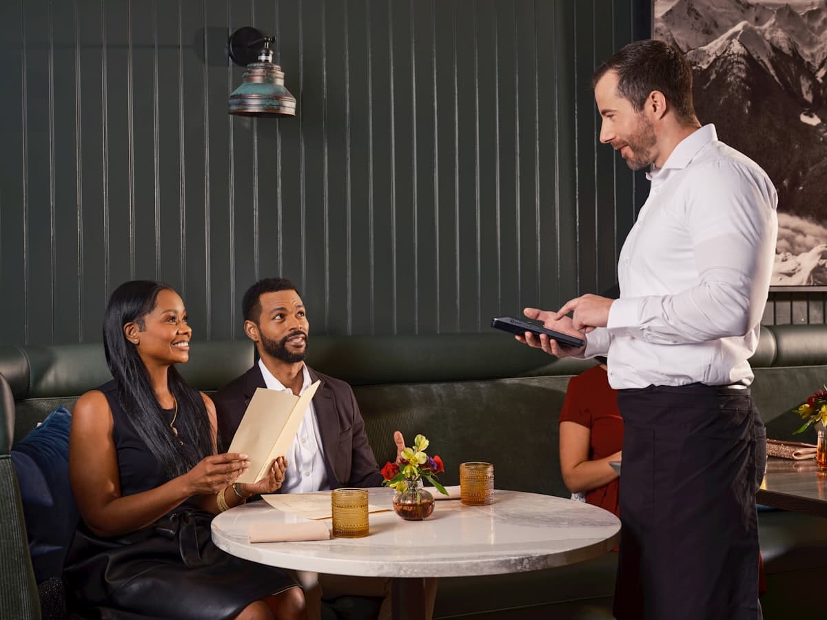 A server with a handheld device talking to guests at their table